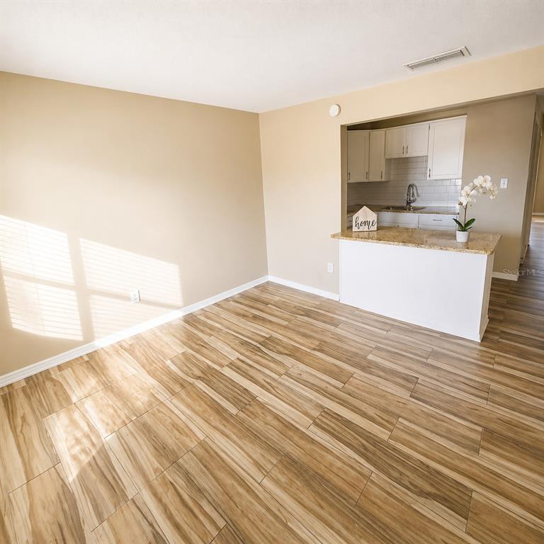 A living area with wood-look tile flooring opens to a kitchen with white cabinets — 2501 HARN BOULEVARD UNIT H27, CLEARWATER, FL