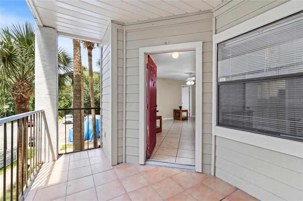 A tiled balcony leads through an open red door into a room with tile flooring — 3032 PARKWAY BOULEVARD UNIT 208, KISSIMMEE, FL