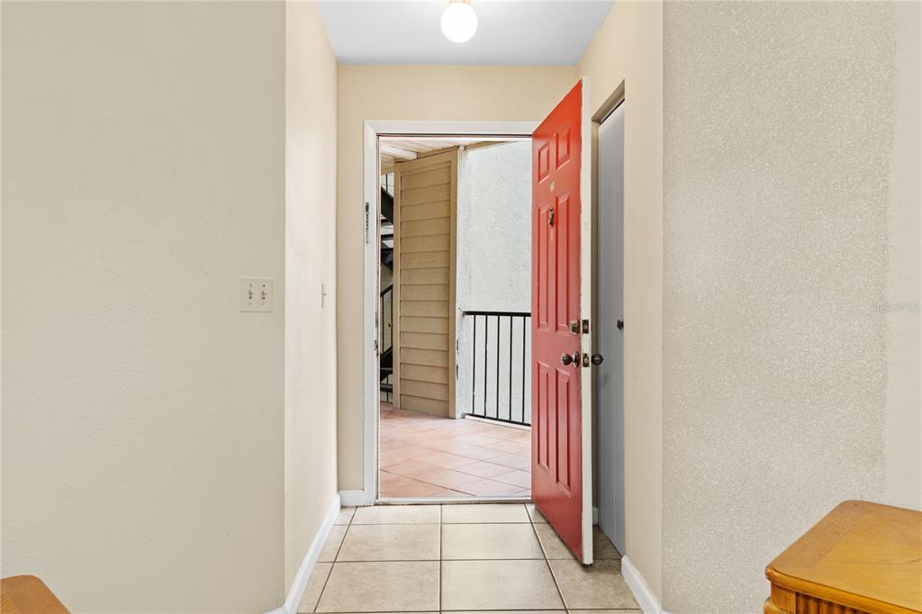 An interior entryway with tiled flooring leads to an open red door and balcony — 3032 PARKWAY BOULEVARD UNIT 208, KISSIMMEE, FL