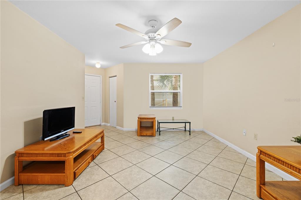 A living room with beige walls, tile flooring, a ceiling fan, and wooden furniture — 3032 PARKWAY BOULEVARD UNIT 208, KISSIMMEE, FL