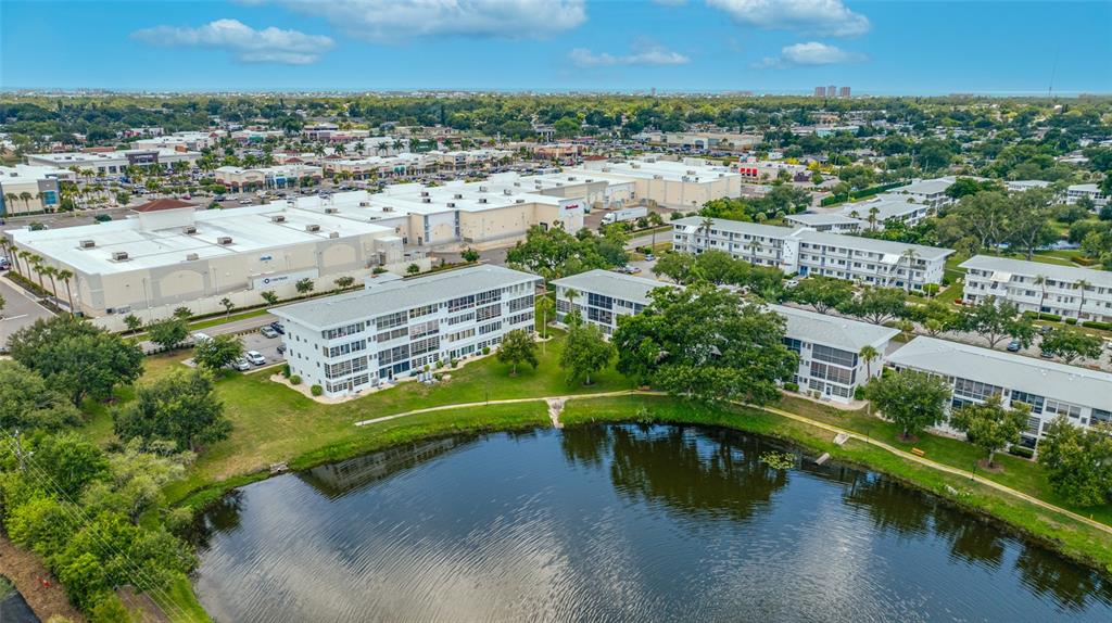 An aerial view shows apartment buildings situated beside a pond near a commercial shopping center — 8075 112TH STREET UNIT 104, SEMINOLE, FL