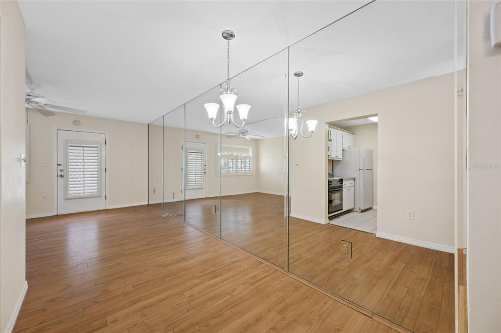 A living room with wood-look flooring and a large mirrored wall reflecting the kitchen area — 8075 112TH STREET UNIT 104, SEMINOLE, FL