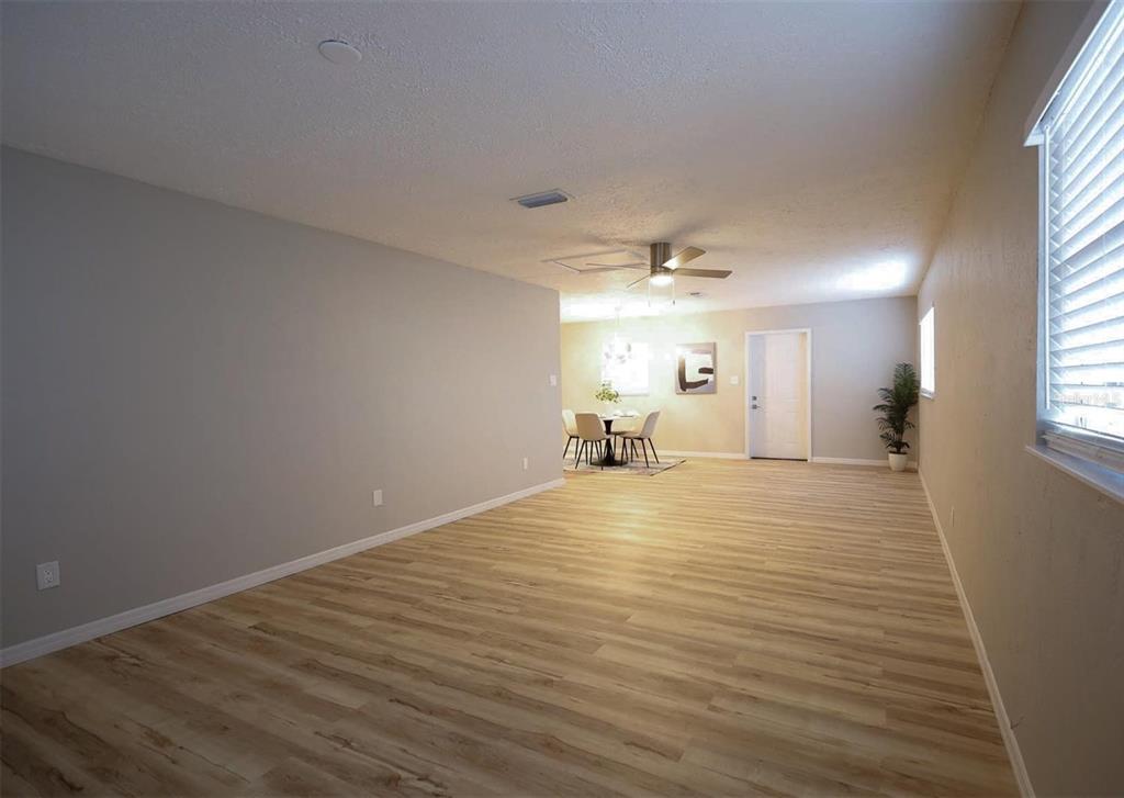 A spacious room with light wood-look flooring, gray walls, and a dining area in back — 3806 W WALLACE AVENUE, TAMPA, FL