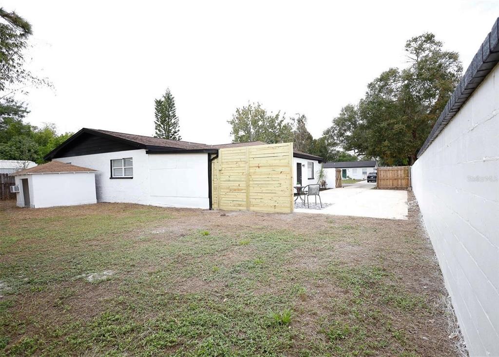 A backyard view showing a white house with a wooden privacy fence and concrete patio — 3806 W WALLACE AVENUE, TAMPA, FL