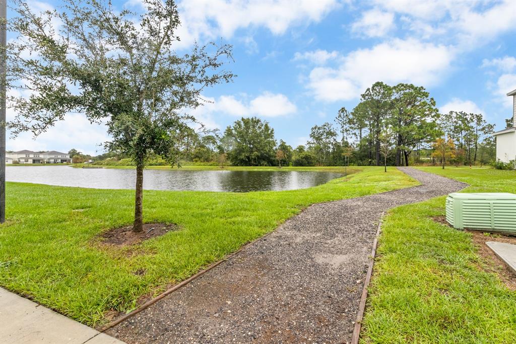 A gravel path winds through a grassy lawn beside a pond and trees — 5674 ARBORVISTA DRIVE, ST CLOUD, FL