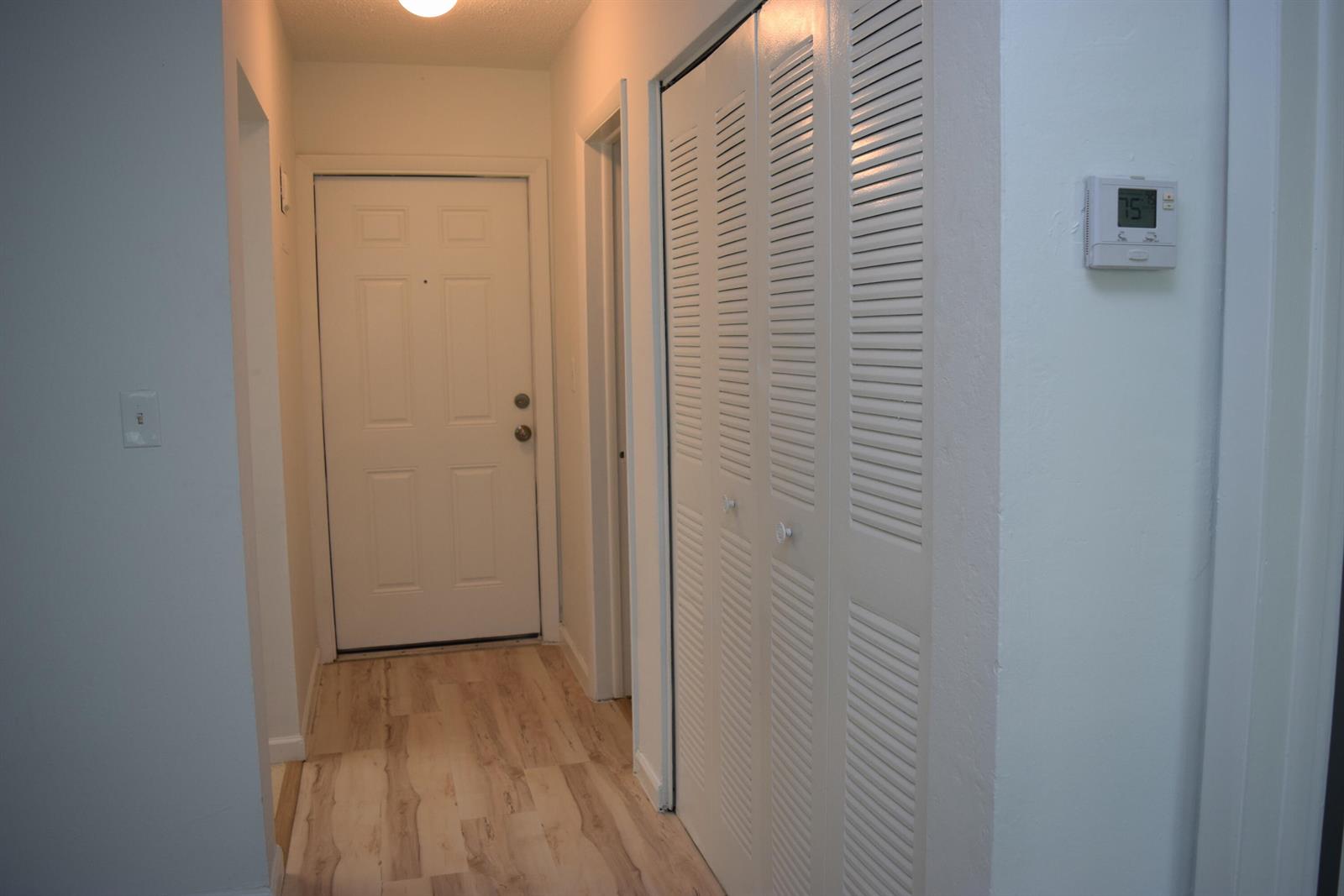 A hallway features light wood-look flooring, a white entry door, and white louvered closet doors — 151 SE 6th Avenue Apt 14, Pompano Beach FL 33060, POMPANO BEACH, FL