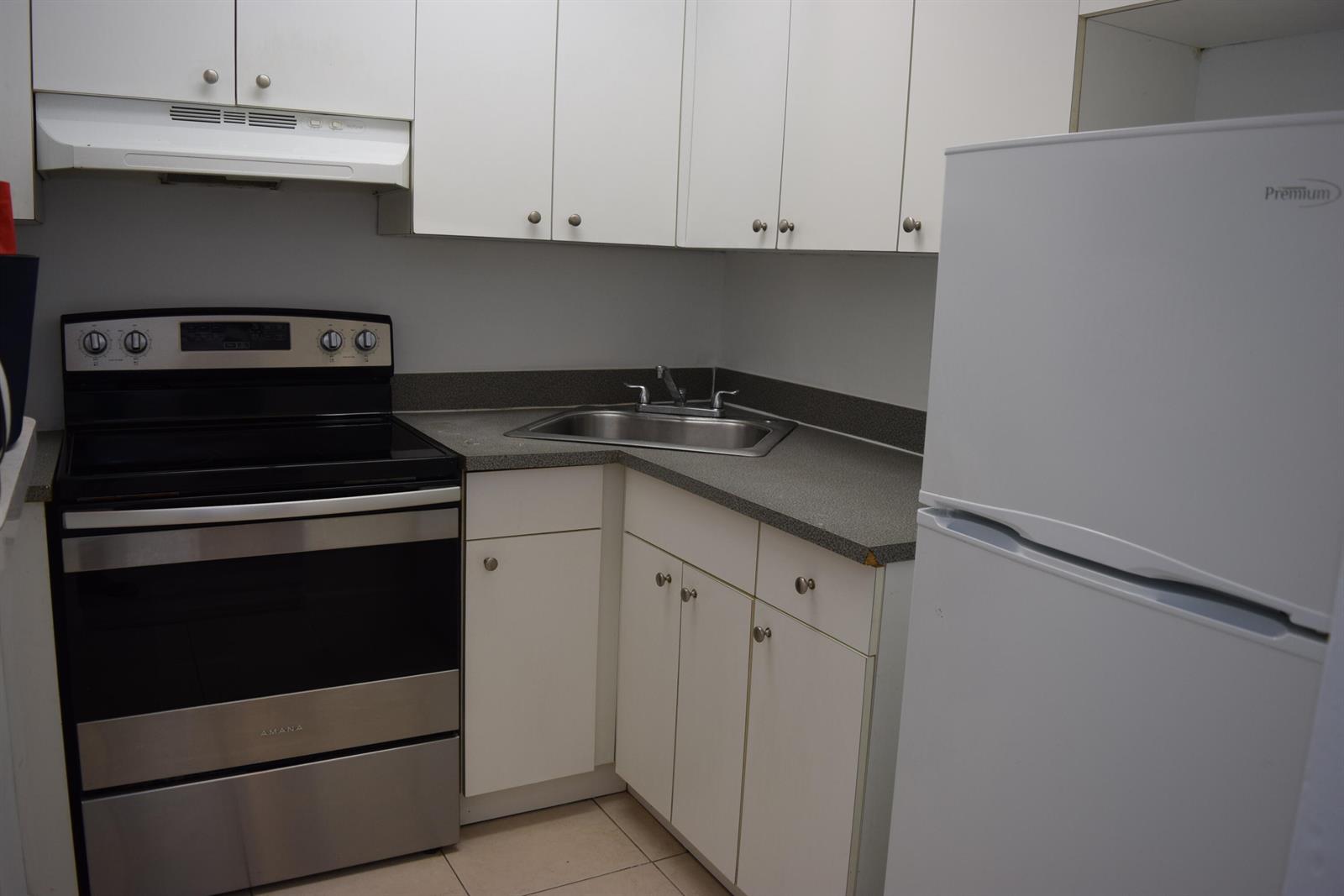 A small kitchen features white cabinets, stainless steel appliances, and a corner sink — 151 SE 6th Avenue Apt 14, Pompano Beach FL 33060, POMPANO BEACH, FL