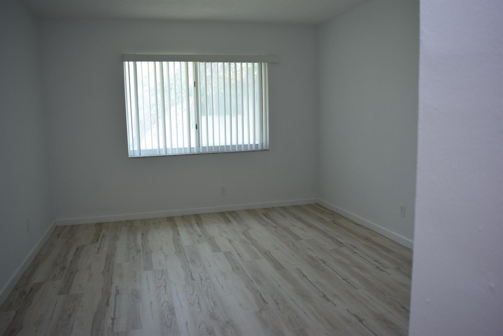 An empty room with white walls, light wood-look flooring, and a window with vertical blinds — 151 SE 6th Avenue Apt 14, Pompano Beach FL 33060, POMPANO BEACH, FL