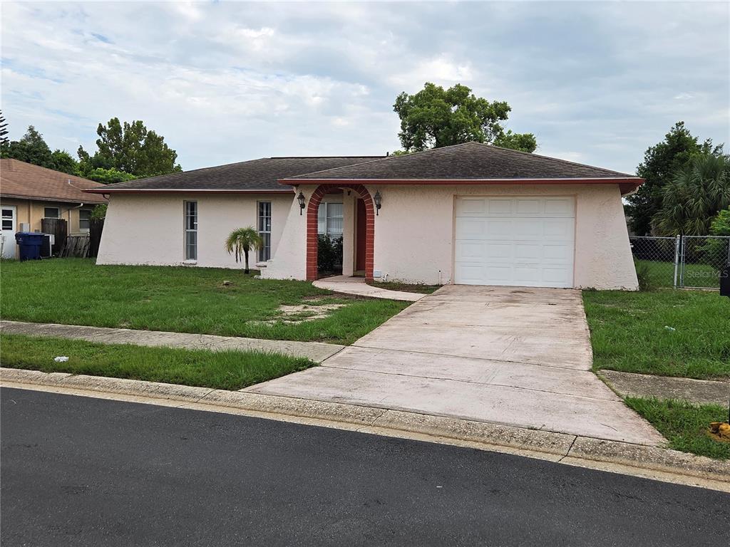 A single-story house with a light-colored stucco exterior, a brick-arched entryway, and a concrete driveway — 7005 PIN CHERRY LANE, PORT RICHEY, FL