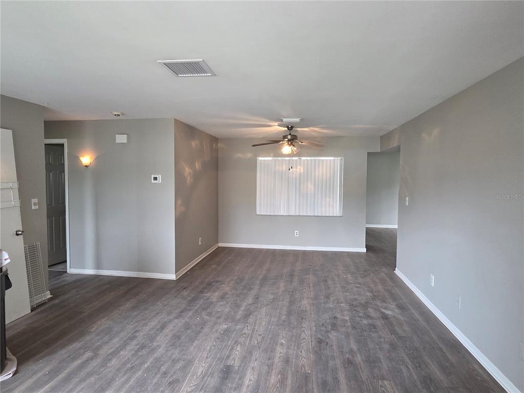 An empty room features gray walls, wood-look flooring, a ceiling fan, and a window with blinds — 7005 PIN CHERRY LANE, PORT RICHEY, FL
