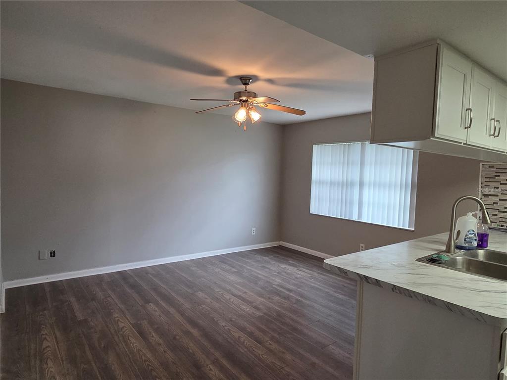 An open-concept living area features wood-look flooring, gray walls, a ceiling fan, and a kitchen counter — 7005 PIN CHERRY LANE, PORT RICHEY, FL