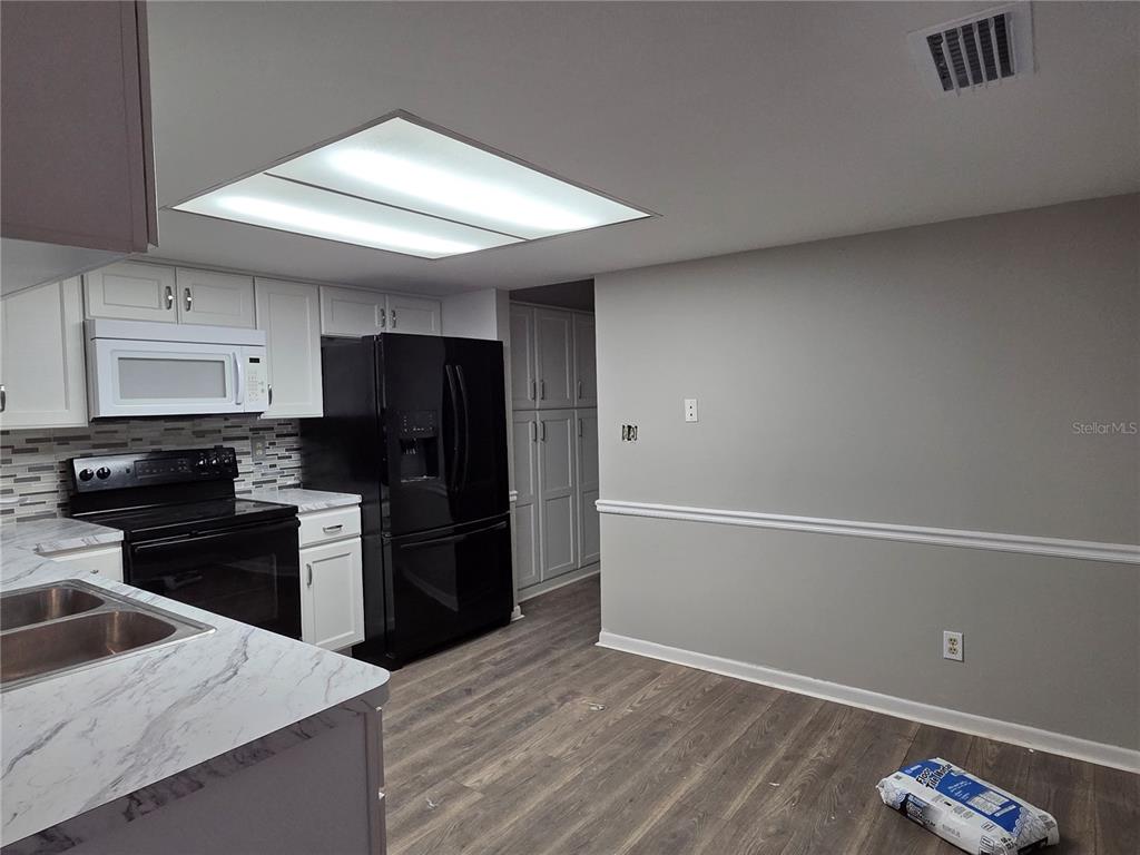 A kitchen features white cabinets, black appliances, marble-look countertops, and wood-style flooring — 7005 PIN CHERRY LANE, PORT RICHEY, FL
