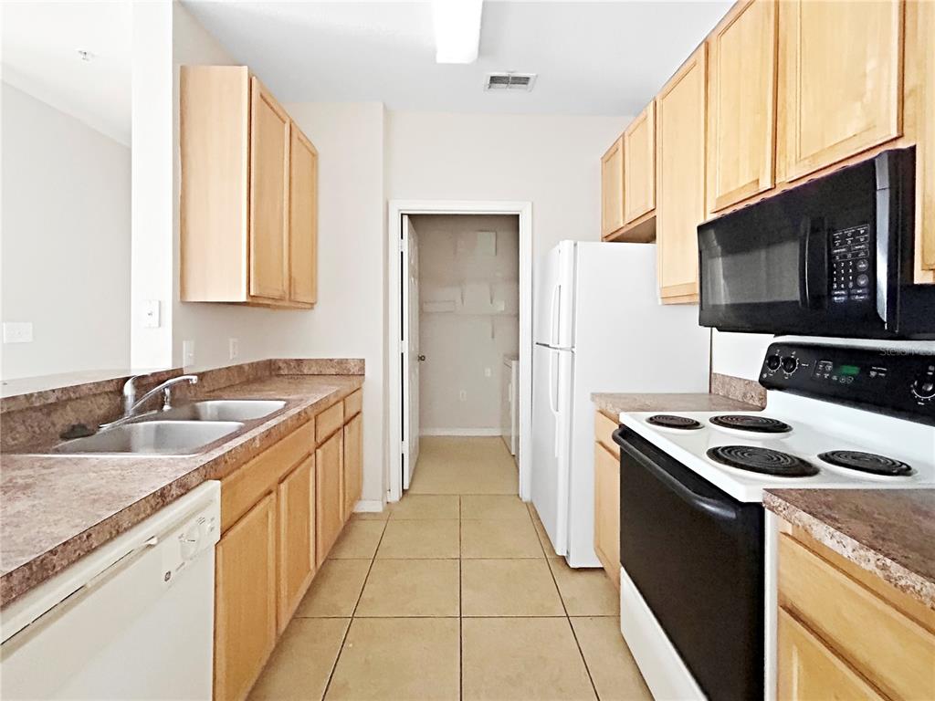 A kitchen features light wood cabinets, laminate countertops, a white dishwasher, and a black stove — 10205 COURTNEY PALMS BOULEVARD UNIT 101, TAMPA, FL
