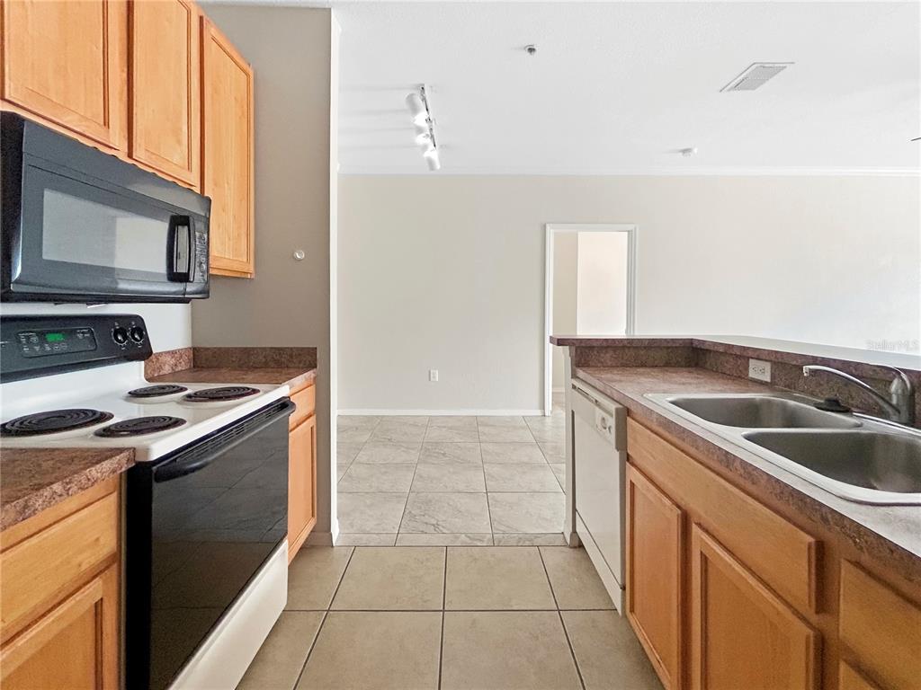 A kitchen features light wood cabinets, dark countertops, a black stove, and tiled flooring — 10205 COURTNEY PALMS BOULEVARD UNIT 101, TAMPA, FL