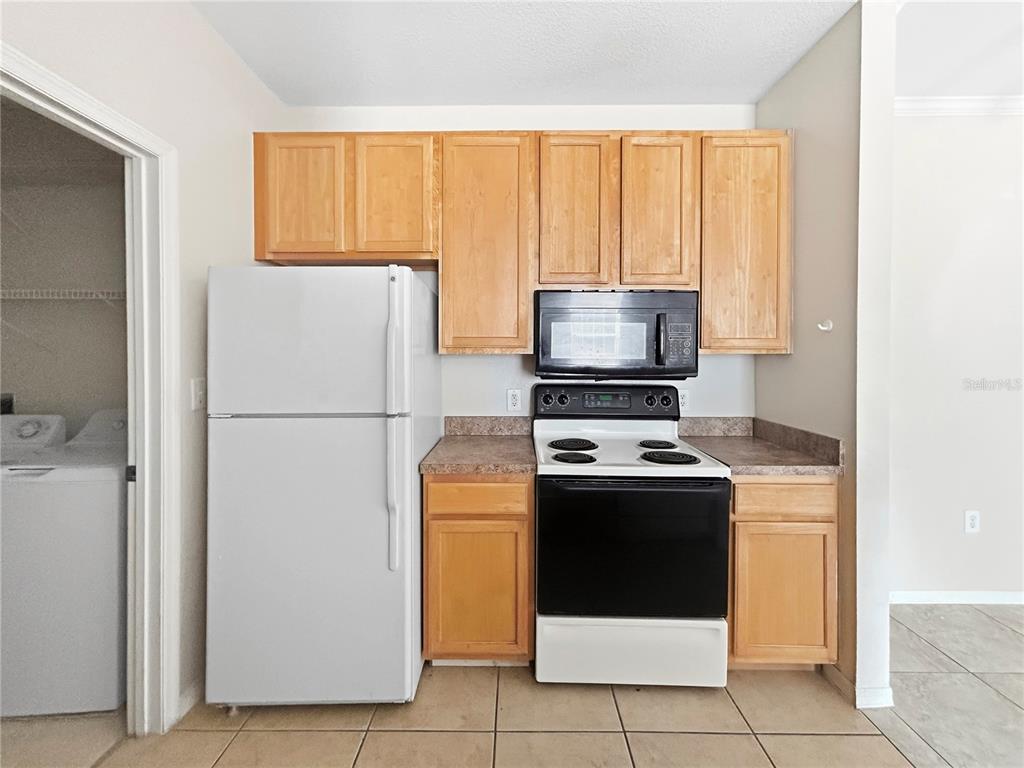 A kitchen features light wood cabinets, a white refrigerator, and a black stove and microwave — 10205 COURTNEY PALMS BOULEVARD UNIT 101, TAMPA, FL