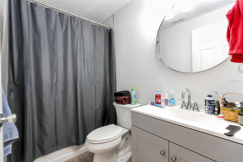A bathroom features a gray vanity, a round mirror, a toilet, and a gray shower curtain — 923 OXFORD STREET, LONGWOOD, FL