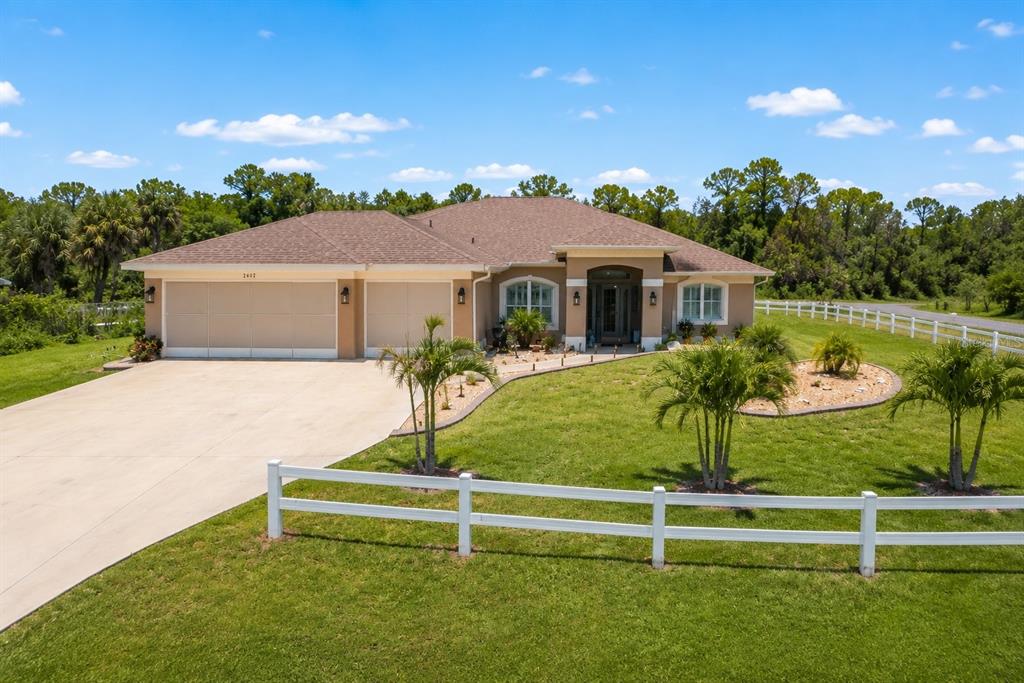 A single-story house with a three-car garage and a white fence sits on a lawn — 2602 YAMADA LANE, NORTH PORT, FL