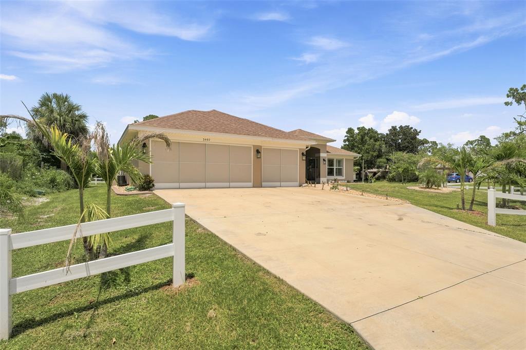 A single-story house with a tan exterior, a three-car garage, and a concrete driveway — 2602 YAMADA LANE, NORTH PORT, FL