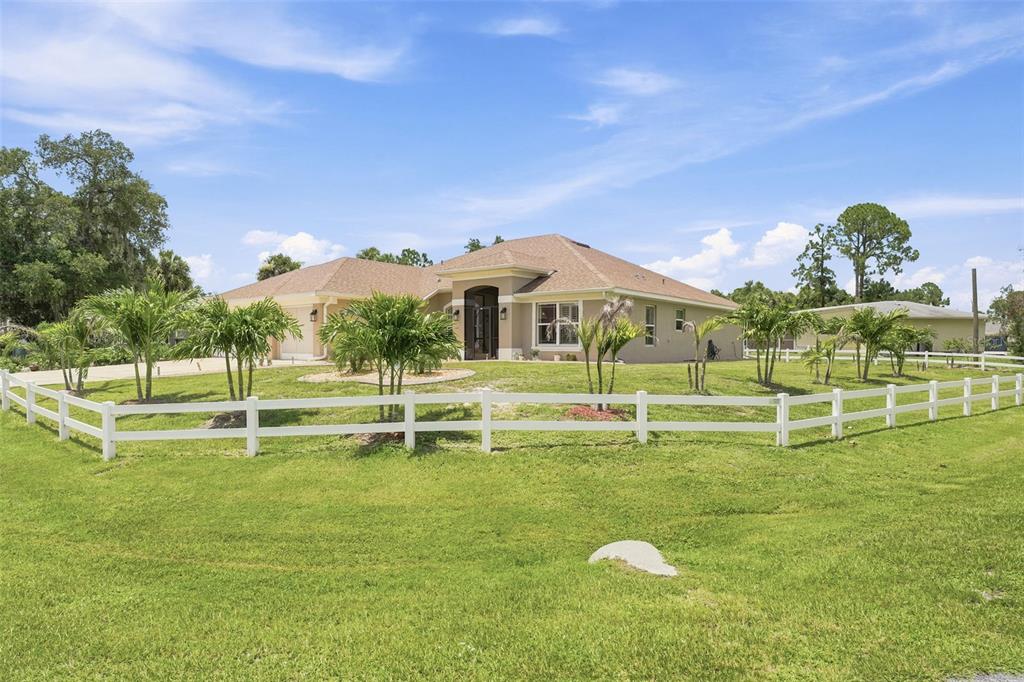 A single-story house with a tan exterior and a white fence sits on a lawn — 2602 YAMADA LANE, NORTH PORT, FL