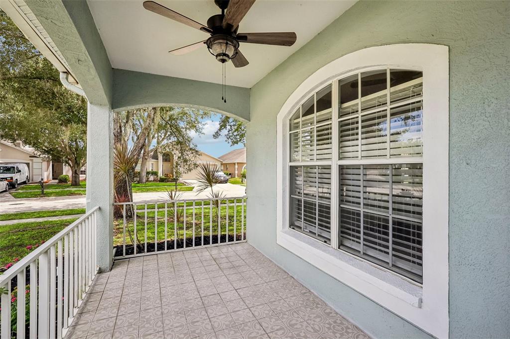 A covered porch features a tiled floor, a ceiling fan, and a white metal railing — 2510 BUTTERFLY LANDING DRIVE, LAND O LAKES, FL