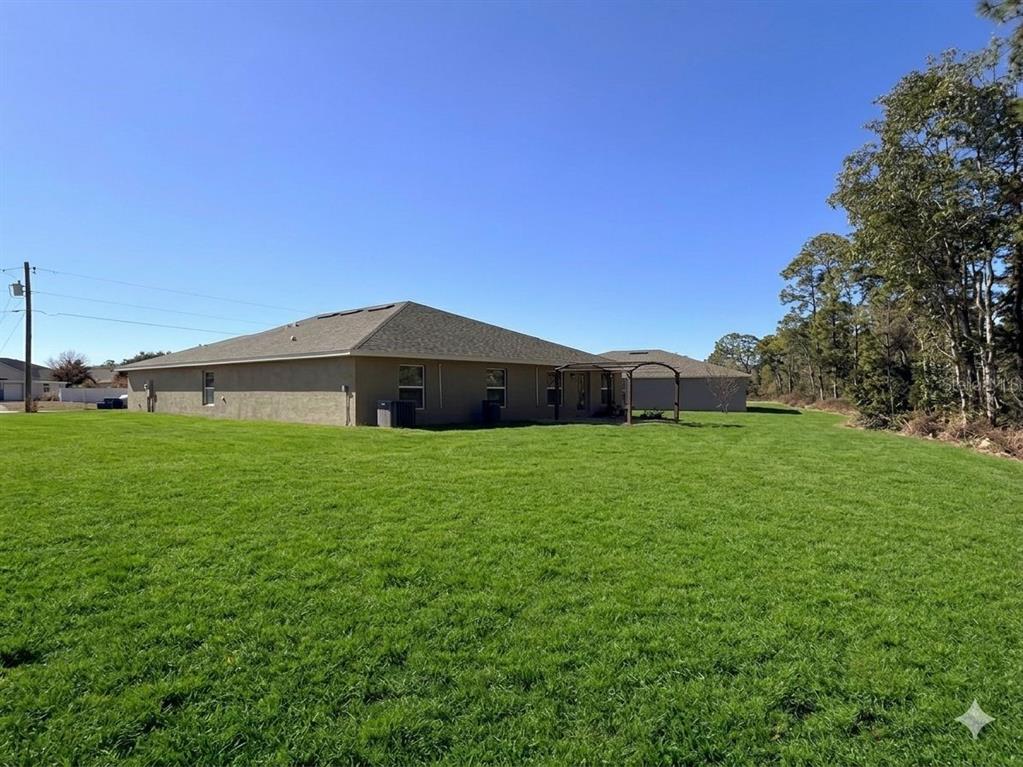 The exterior of a tan house with a large green lawn and trees — 910 HUDSON VALLEY DRIVE, KISSIMMEE, FL