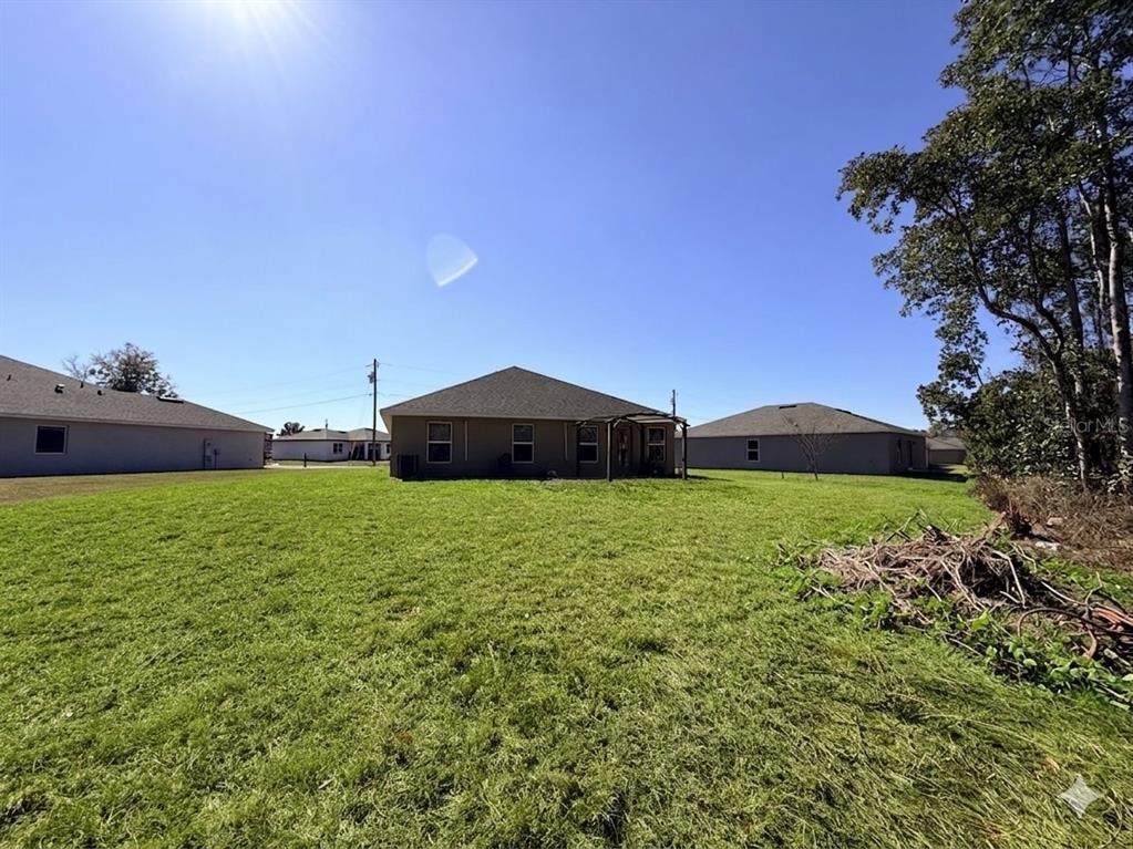 The rear exterior view of a single-story house features a large grassy backyard — 910 HUDSON VALLEY DRIVE, KISSIMMEE, FL