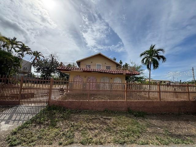 A two-story house with a balcony and a metal fence stands under a cloudy sky — Calle 8 BO. PIEDRA AGUZA UNIT Casa 8, JUANA DIAZ, PR