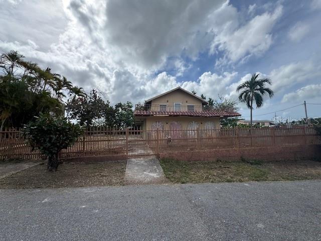 A two-story house with a balcony and a fenced yard stands under a cloudy sky — Calle 8 BO. PIEDRA AGUZA UNIT Casa 8, JUANA DIAZ, PR