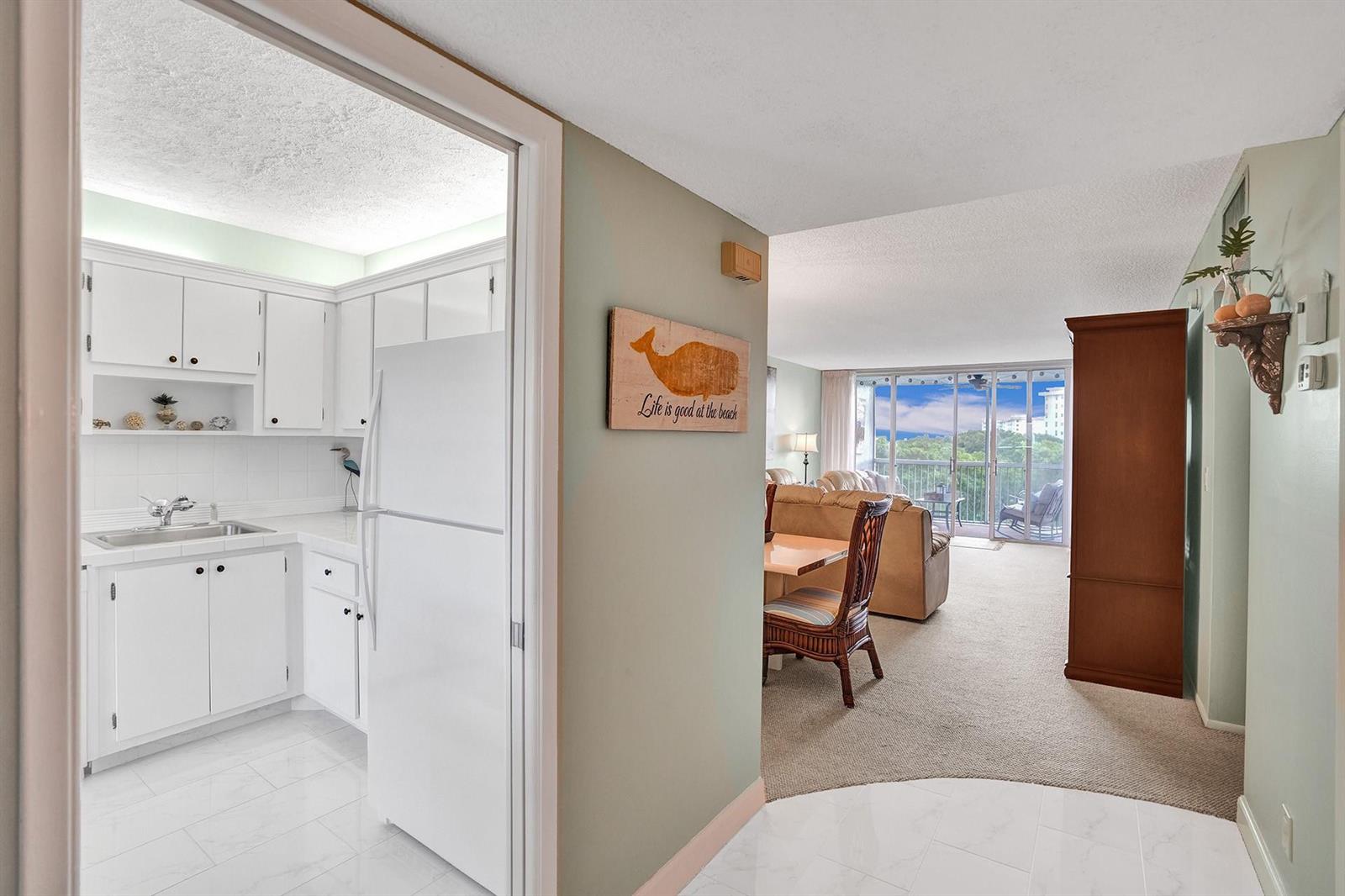 A view from a tiled entryway looking into a white kitchen and a carpeted living area — 2940 N Course Drive # 511, Pompano Beach FL 33069, POMPANO BEACH, FL