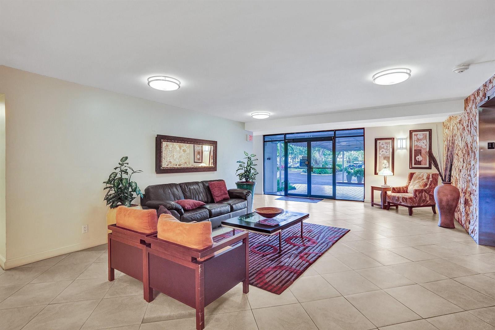 A lobby features a dark leather sofa, two orange armchairs, a patterned rug, and tile flooring — 2940 N Course Drive # 511, Pompano Beach FL 33069, POMPANO BEACH, FL