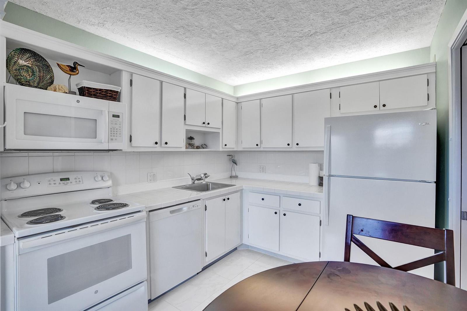 A kitchen with white cabinets, white appliances, tiled countertops, and a popcorn ceiling — 2940 N Course Drive # 511, Pompano Beach FL 33069, POMPANO BEACH, FL