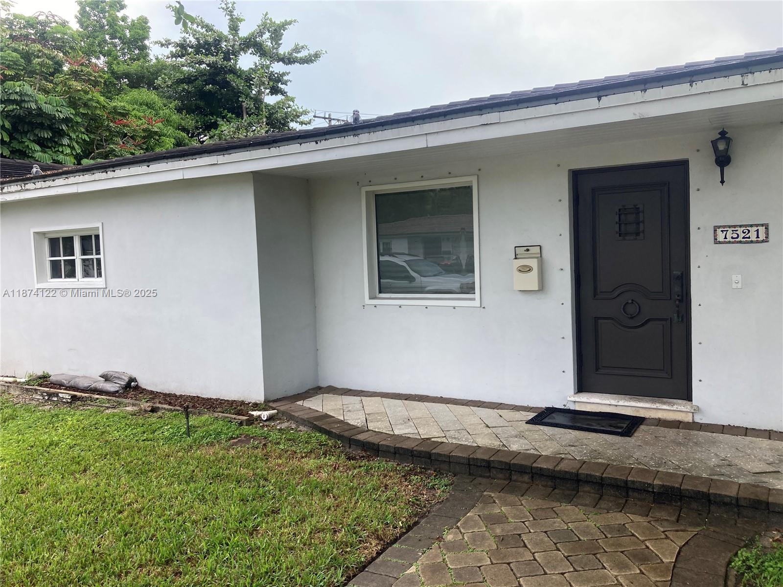 The exterior of a white house features a dark front door and a paved walkway — 7521 SW 57th Ter, Miami FL 33143, MIAMI, FL