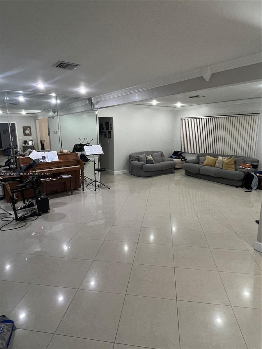 A spacious living room features light tile flooring, mirrored walls, a piano, and two sofas — 7521 SW 57th Ter, Miami FL 33143, MIAMI, FL