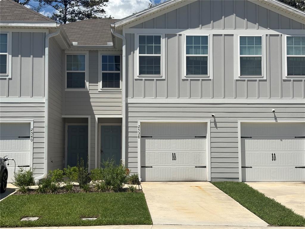 A two-story townhouse exterior features gray vertical and horizontal siding with two white garage doors — 2538 SADLER TRACE WAY, JACKSONVILLE, FL