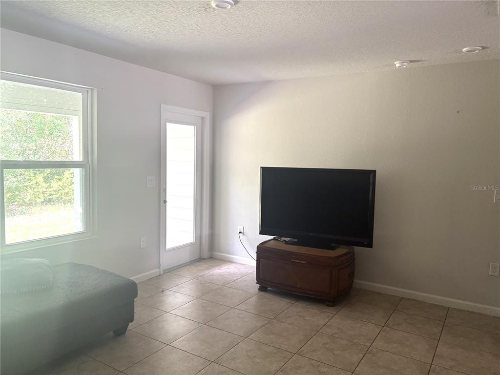 A living room features tile flooring, a television on a wooden stand, and a glass door — 2538 SADLER TRACE WAY, JACKSONVILLE, FL