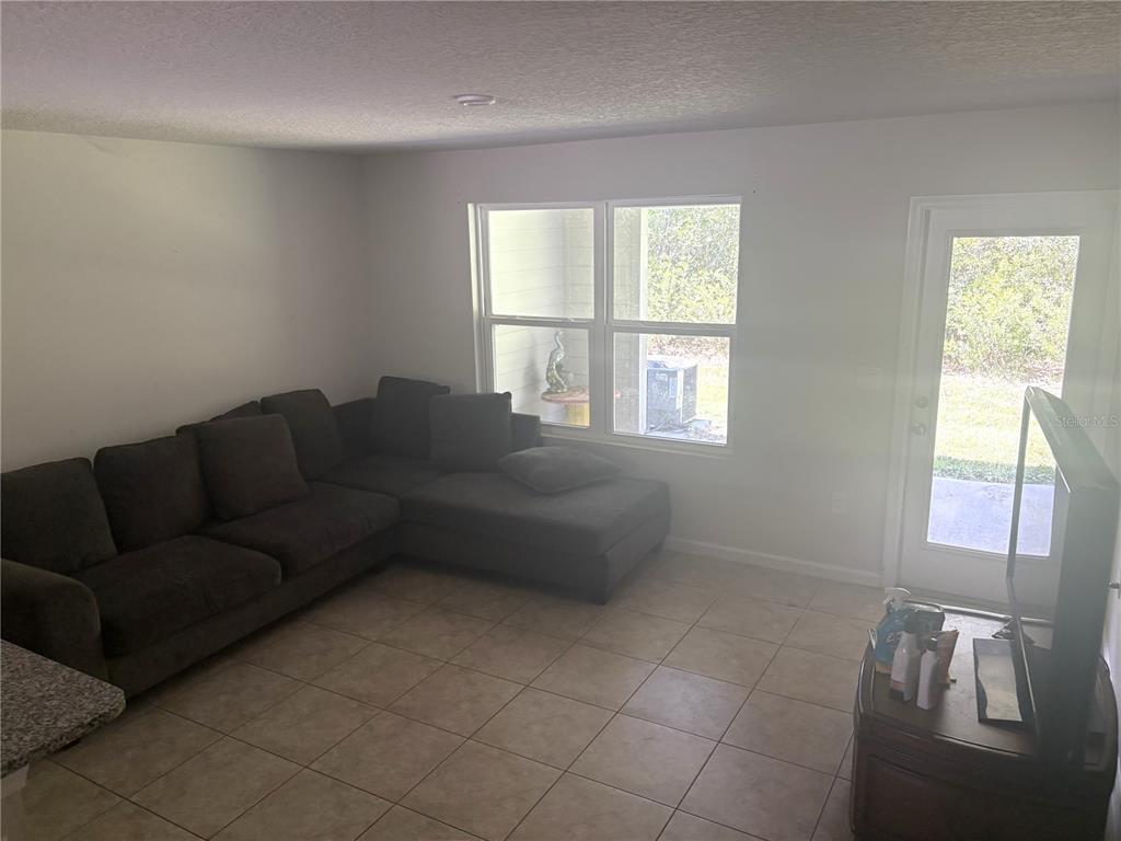 A living room features a dark sectional sofa, tile flooring, a window, and a glass door — 2538 SADLER TRACE WAY, JACKSONVILLE, FL