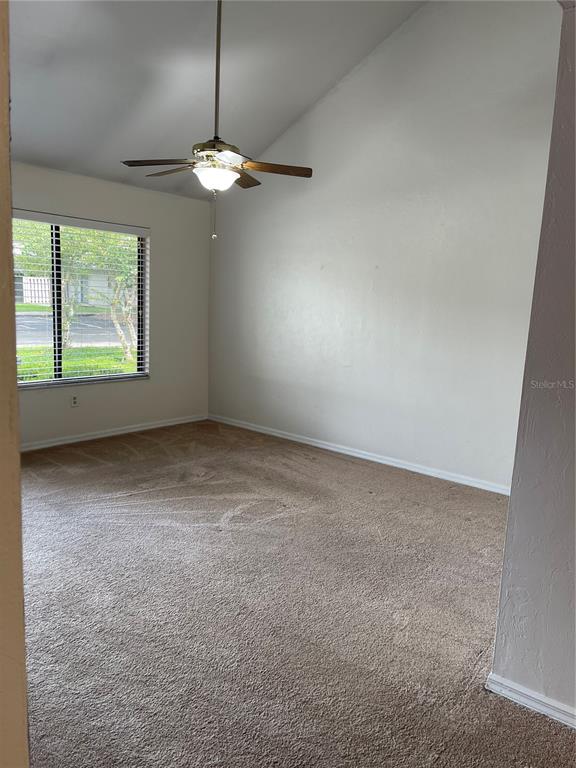 An empty room features beige carpet, white walls, a vaulted ceiling, and a ceiling fan — 3504 NW 37TH AVENUE, GAINESVILLE, FL