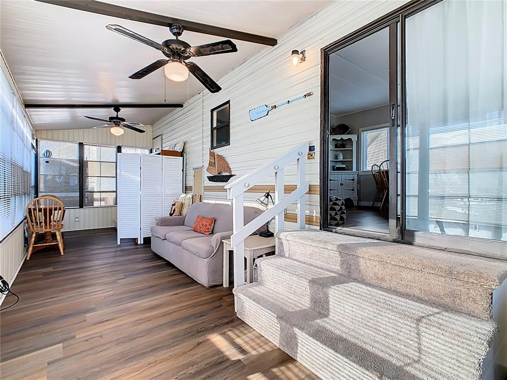 A sunroom features wood-look flooring, a sofa, ceiling fans, and carpeted stairs leading inside — 9000 US HWY 192 UNIT 296, CLERMONT, FL