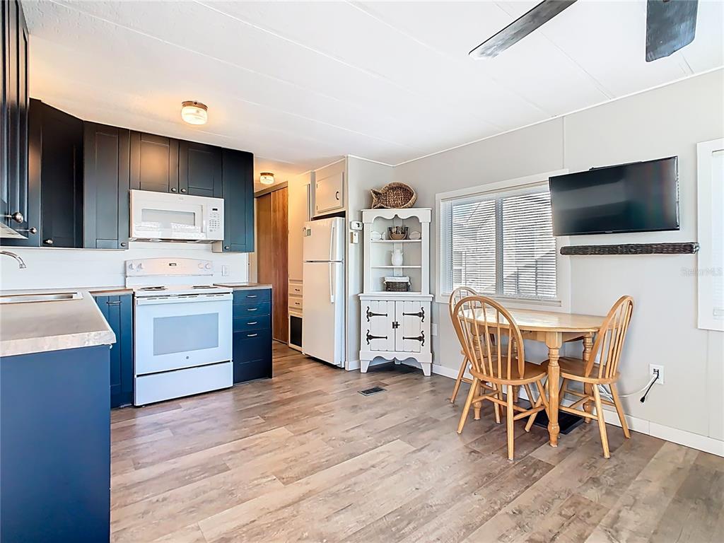 A kitchen and dining area with dark blue cabinets, white appliances, and wood-look flooring — 9000 US HWY 192 UNIT 296, CLERMONT, FL