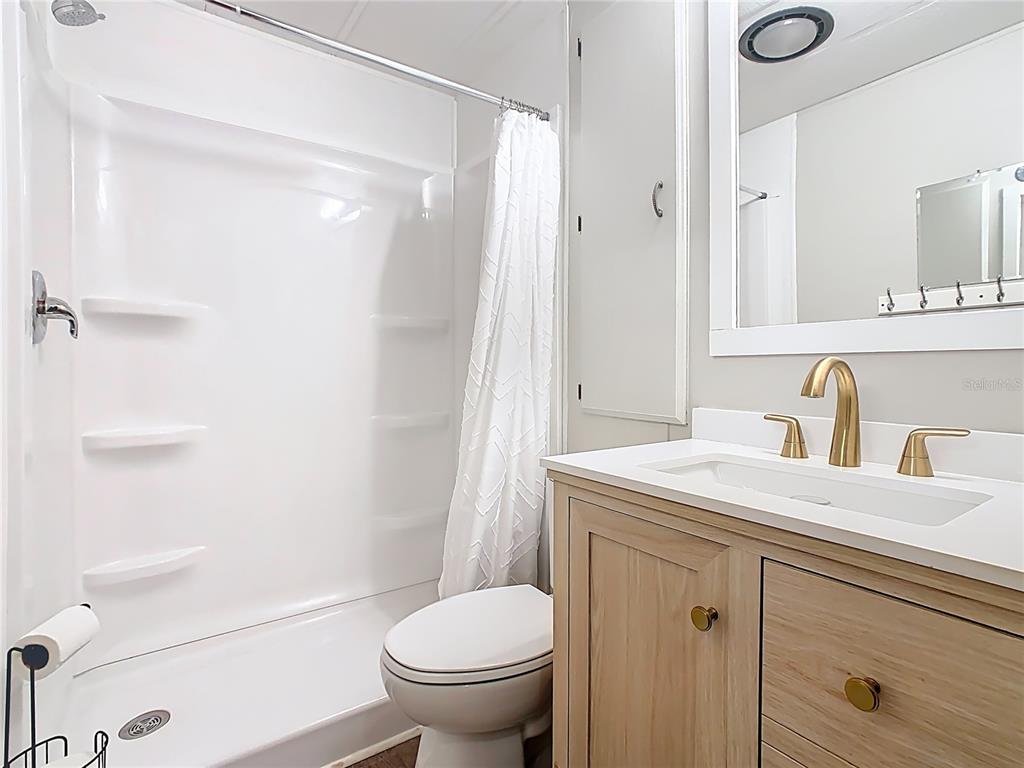 A bathroom features a white shower stall, a toilet, and a wood vanity with gold fixtures — 9000 US HWY 192 UNIT 296, CLERMONT, FL