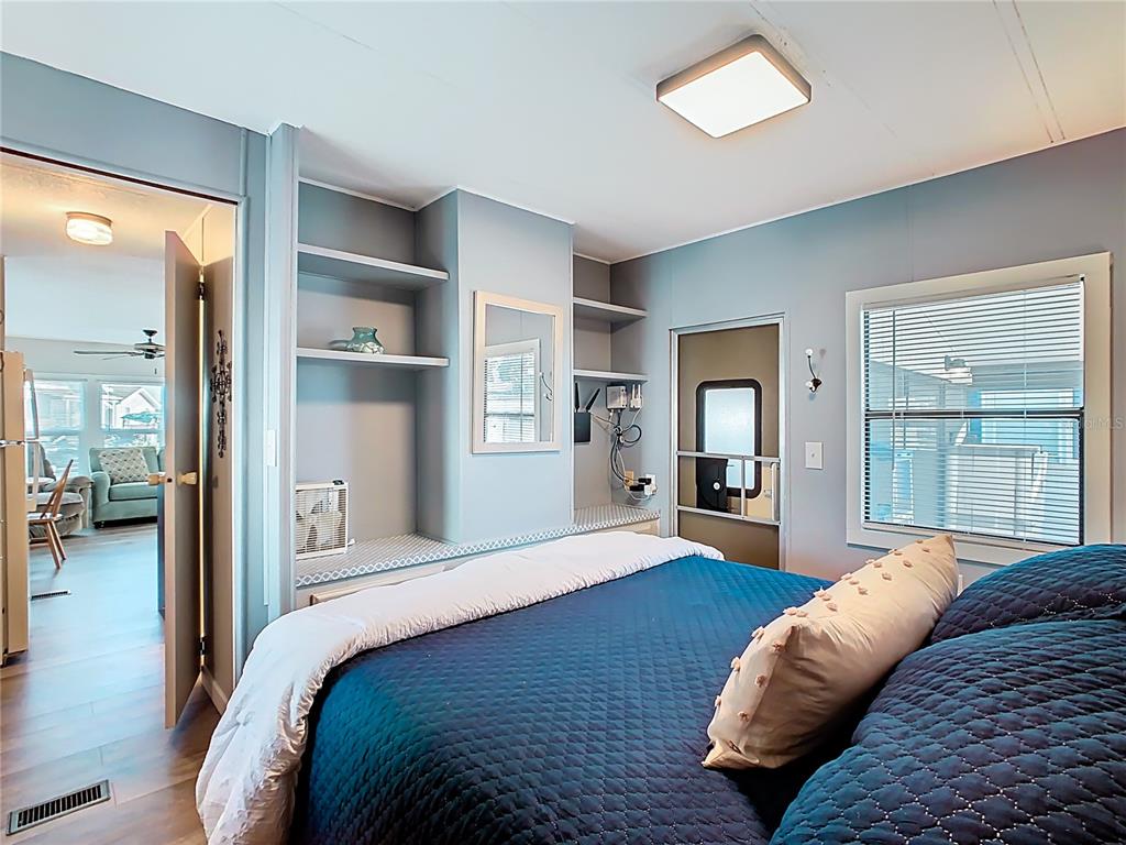 A bedroom features a blue bed, built-in shelving, a window with blinds, and a doorway — 9000 US HWY 192 UNIT 296, CLERMONT, FL