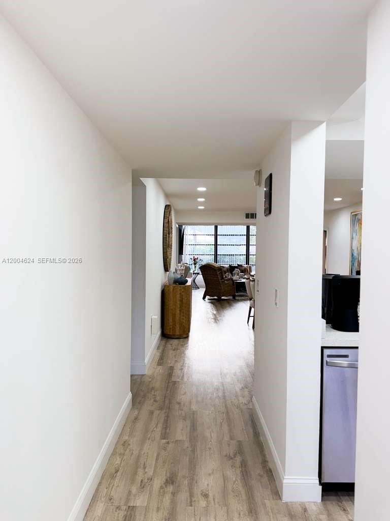 A hallway with light wood-look flooring leads toward a living area with large windows — 1721 Whitehall Dr # 101, Davie FL 33324, DAVIE, FL