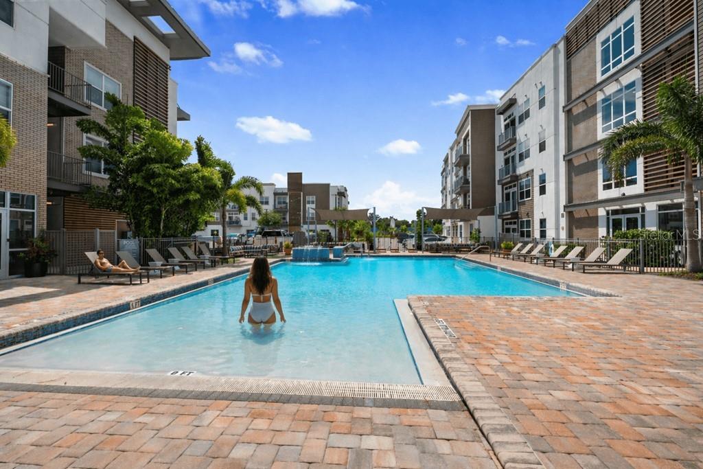 A woman stands in a rectangular swimming pool surrounded by a brick patio and apartment buildings — 1185 S PINELLAS AVENUE UNIT B1, TARPON SPRINGS, FL