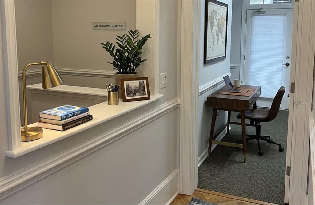 A reception area with a desk, books, and a plant leads to a small office — 5214 SW 91ST TERRACE UNIT A, GAINESVILLE, FL