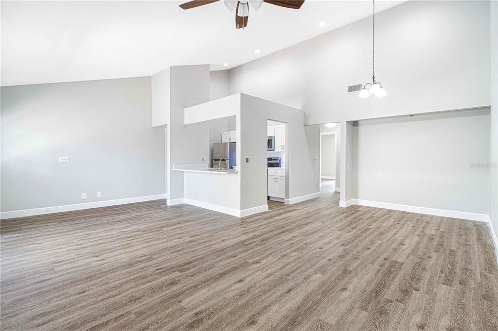 A spacious living room with vaulted ceilings, wood-look flooring, and an open kitchen pass-through — 4111 SE 22ND AVENUE, OCALA, FL