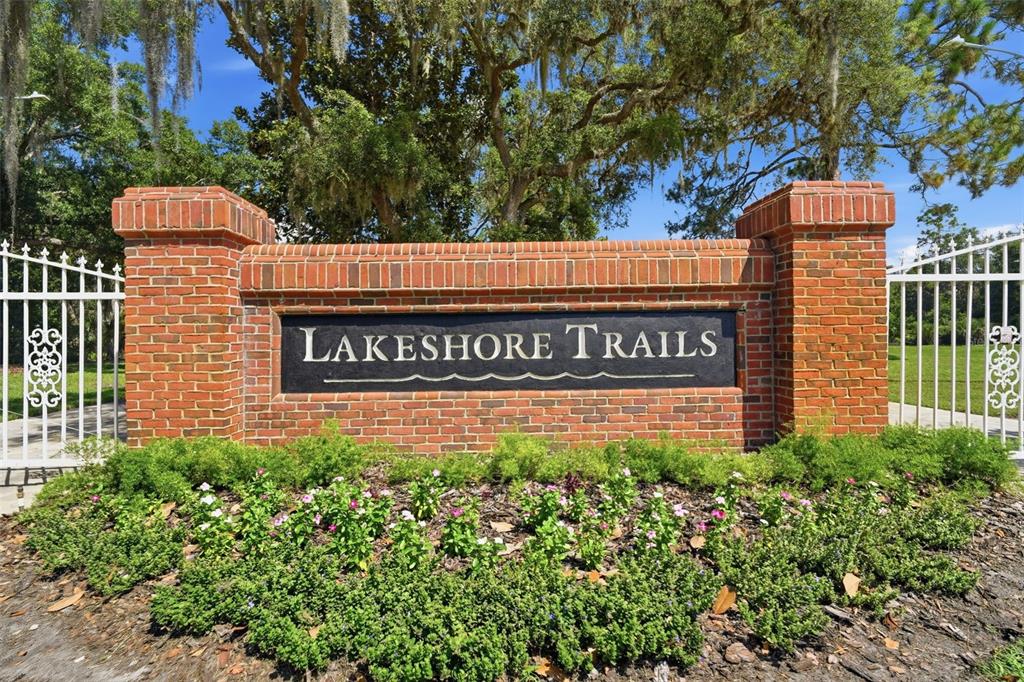 A brick monument sign for Lakeshore Trails stands in front of trees and white fencing — 687 WINTERBERRY TRAIL, DELAND, FL