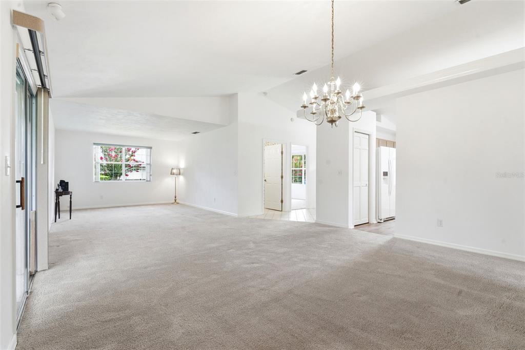 A spacious living room features neutral carpeting, white walls, a chandelier, and sliding glass doors — 687 WINTERBERRY TRAIL, DELAND, FL