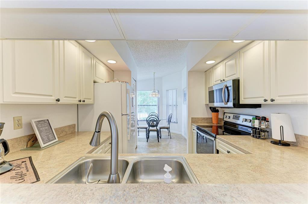 A kitchen with white cabinets, laminate countertops, and a stainless steel sink overlooks a dining area — 4320 47TH AVENUE W UNIT 204, BRADENTON, FL