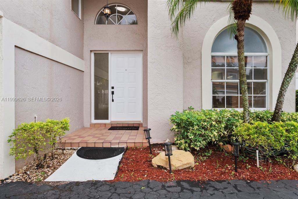 The exterior of a house features a white front door, arched windows, and landscaping — 7685 NW 62nd Way, Parkland FL 33067, PARKLAND, FL