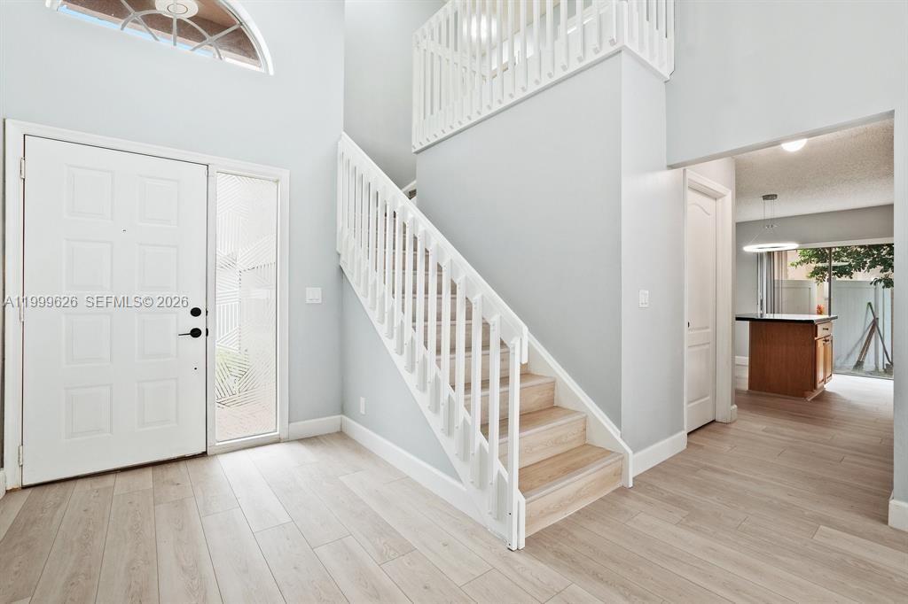 A bright entryway features light wood-look flooring, a white staircase, and a high ceiling — 7685 NW 62nd Way, Parkland FL 33067, PARKLAND, FL